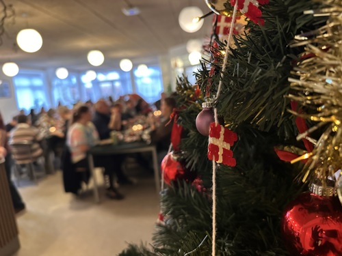 Gæster til julefrokost bagved et juletræ med pynt