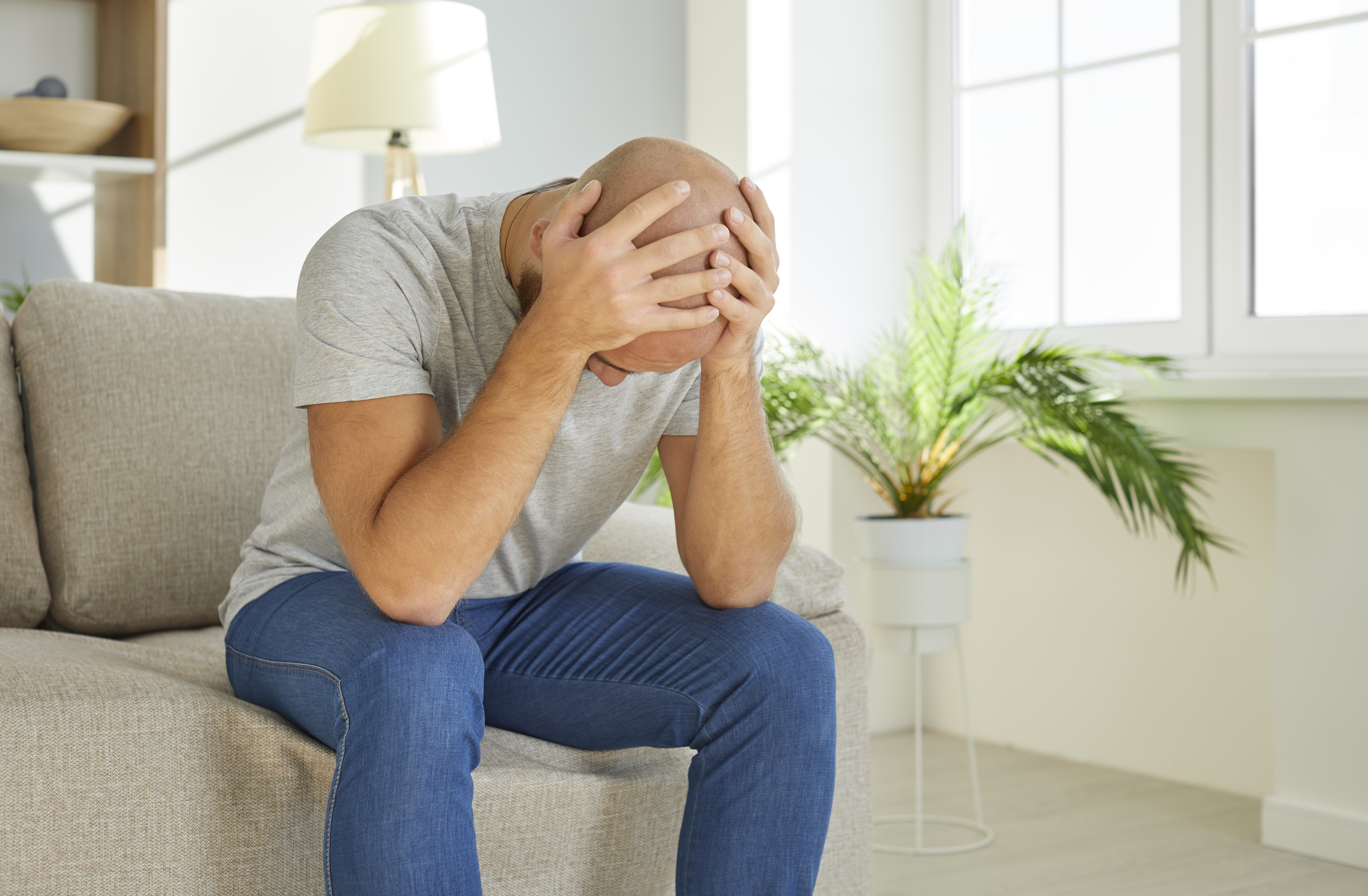 Foto af en mand, der sidder på en sofa og tager sig til hovedet